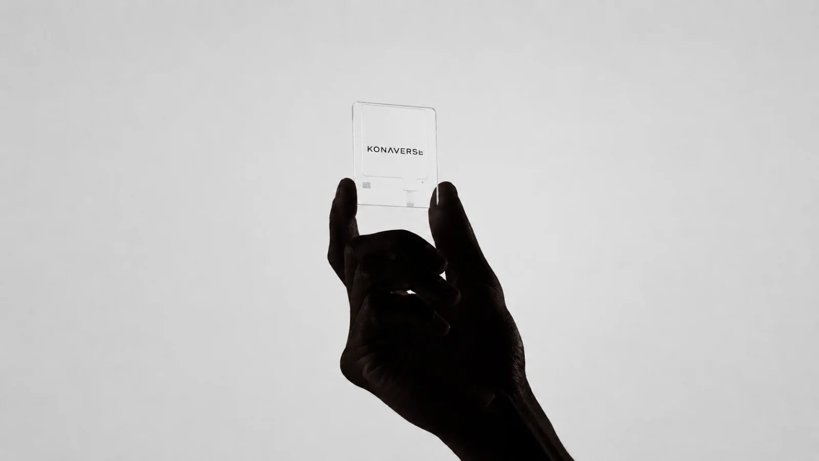 A hand holding a glass card engraved with the Konaverse logo